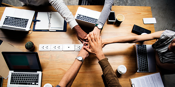 Equipe de trabalho com as mãos unidas sobre a mesa com computadores e agendas